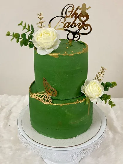 This two-tier baby shower cake in a rich emerald green is a unique and elegant choice. Accented with gold trim, golden butterflies, and white roses, it's a sophisticated way to celebrate a new arrival.
