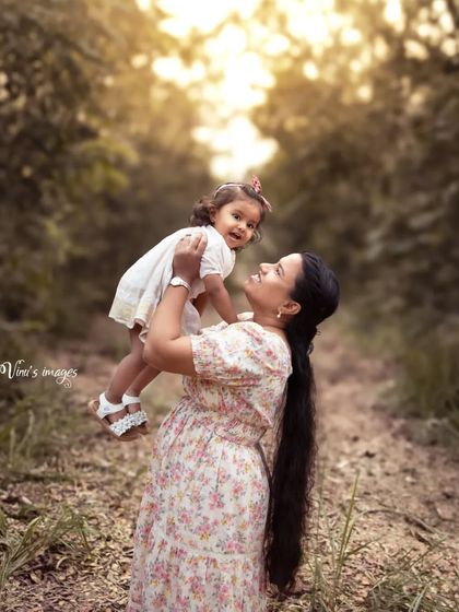 A mother lifts her daughter up in the air, both sharing a look of pure happiness. This outdoor shot is full of life, love, and beautiful natural light.