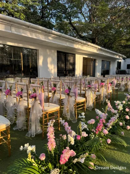 Every detail is considered, including guest seating. Here, chairs are decorated with delicate tulle and fresh pink flowers, complementing the floral arrangements that line the aisle for a cohesive and beautiful ceremony design.