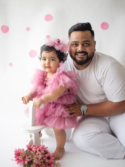 A proud father with his daughter on her first birthday. Their matching smiles make this a heartwarming family photograph.