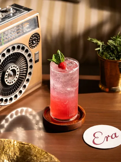 A pink gin and tonic with a raspberry garnish, styled with a retro radio. The composition creates a nostalgic and relaxed atmosphere.