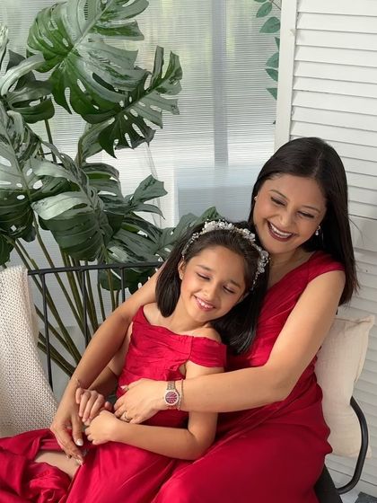 A mother and daughter in matching red dresses share a warm hug.