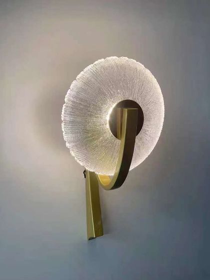A modern wall sconce with a textured glass ring on a brass arm. This design is both elegant and contemporary.