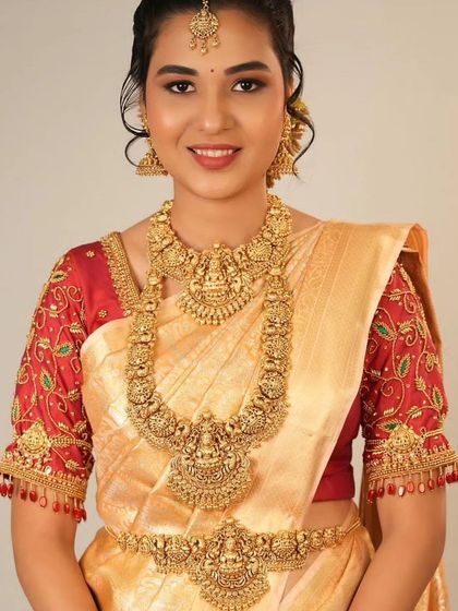 A smiling bride in a silk saree wearing a complete antique-finish temple jewellery set. This includes the choker, long necklace, and waist belt.