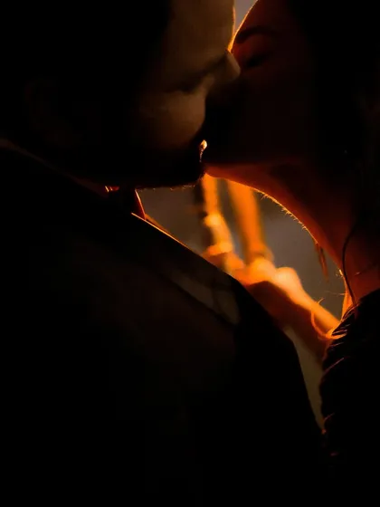 An intimate, shadowy kiss illuminated by a warm, single light source. This low-light photography creates a moody, passionate, and intensely private feeling.