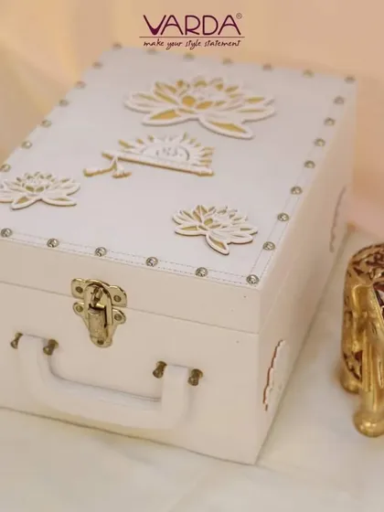 This elegant white trunk-style box is adorned with golden lotus motifs. It's a versatile and luxurious keepsake box that can be used for wedding invitations, trousseau packing, or as a decorative storage piece.