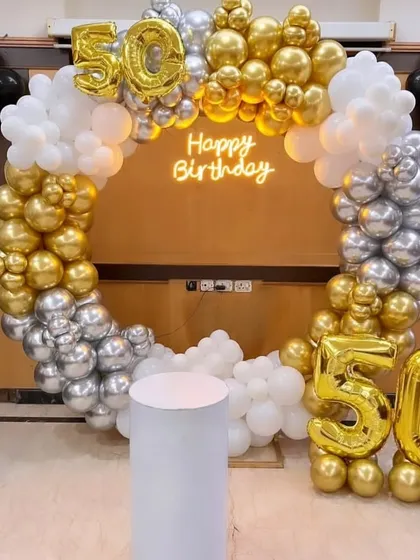 A grand setup for a 50th birthday celebration. The circular balloon arch is made with chrome gold, silver, and white balloons and features large foil numbers to mark the milestone.