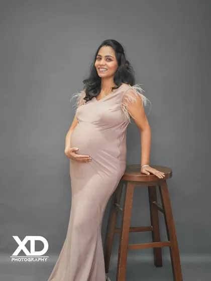 A simple and elegant solo maternity portrait against a clean grey studio background.