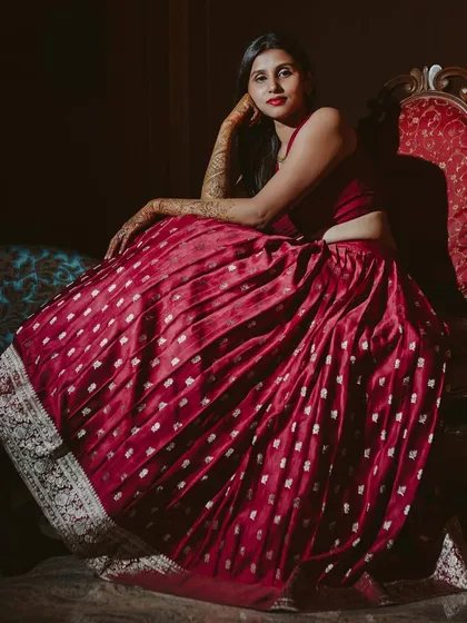 A bride looking regal in a deep red Banarasi lehenga. This dramatic, full-length shot highlights the richness of the fabric and the simplicity of her modern blouse.