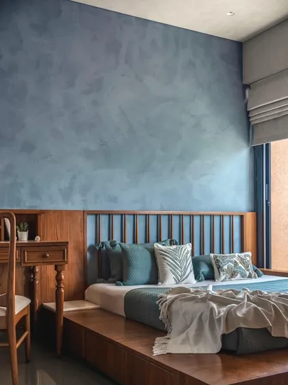 A serene bedroom featuring a beautiful blue lime-washed accent wall, which provides a calming backdrop to the warm wooden platform bed.