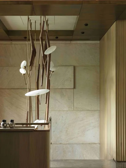 A perspective of the entrance staircase at the Bammi Residence, showing the relationship between the sculptural light, the textured stone wall, and the clean lines of the wooden paneling. The design balances complexity with restraint.