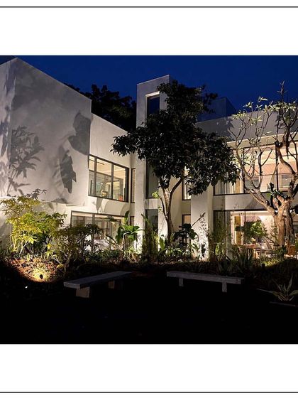 An outdoor retreat corner of a home overlooking forestry in Alibaug. The strategic night lighting creates dramatic shadows and highlights the architectural forms against the natural backdrop.