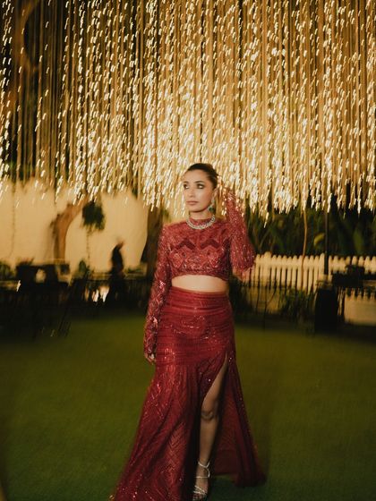 The bride stands under a canopy of lights, her red reception outfit glittering. This is how you create an unforgettable party look.