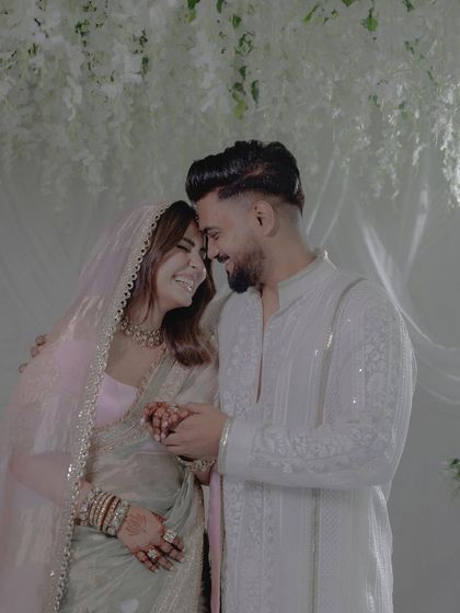 A happy, intimate moment shared by the couple. The soft, diffused lighting and the pure white floral decor enhance the romantic and heartfelt nature of the photograph.
