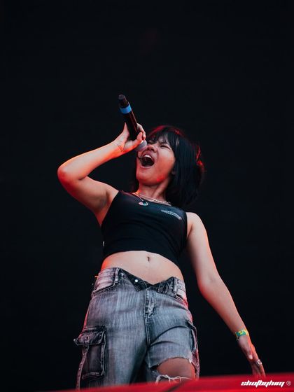 Kim the Beloved in a moment of pure performance, singing passionately into the microphone at Rolling Loud India. The clean black background makes her the sole focus.