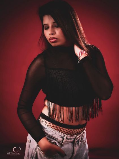 An edgy and modern studio portrait. The combination of a sheer fringe top, fishnets, and ripped jeans creates a cool, layered look against the dramatic red light.