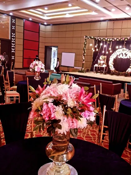 A navy blue themed cocktail or Sangeet event. The decor features dark blue tablecloths and a stage with a floral wreath backdrop, showing how we use deep colors to create a sophisticated evening atmosphere.