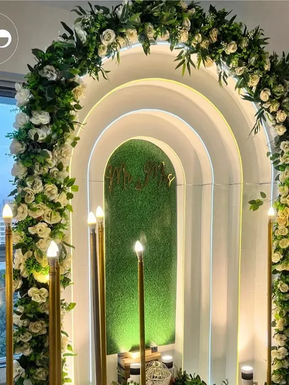 For an intimate home ceremony, we designed this modern and romantic backdrop. The layered arches, soft backlighting, and a lush floral garland of white roses created a dreamy focal point for the couple to exchange their promises.