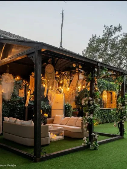 A cozy and chic lounge area for a bohemian-themed event. The curved sofa is placed in a custom-built cabana decorated with macrame dreamcatchers and climbing white roses.