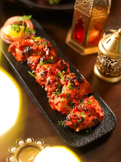Juicy chicken tikka kebabs served on a black platter, with the warm glow of a diya in the background. The festive, moody lighting makes this a perfect shot for a Diwali menu.