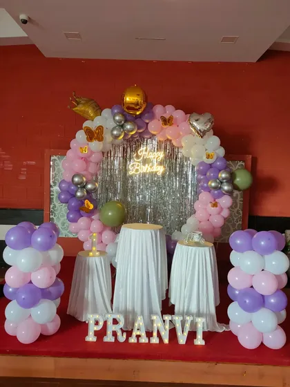 A pastel balloon ring in purple, pink, and white with a silver tinsel curtain.
