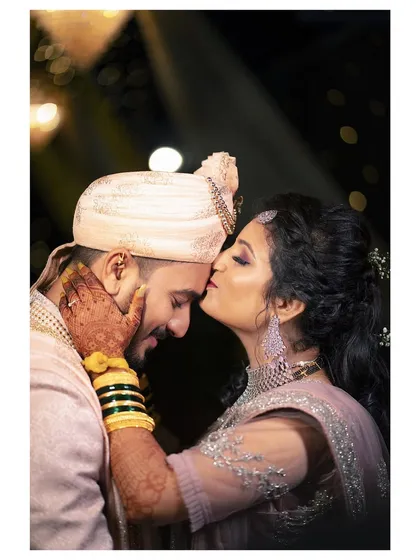 A quiet moment of affection. The groom's gentle kiss on the bride's forehead is a timeless expression of love that we love to capture. This candid wedding portrait highlights the couple's connection amidst the celebration.