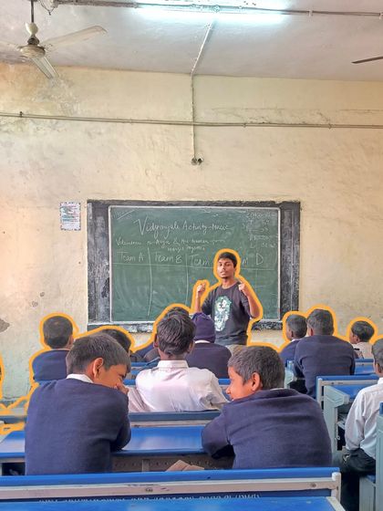 An instructor divides the class into teams for a musical game, with the scores written on the blackboard. This friendly competition makes learning fun and encourages teamwork.