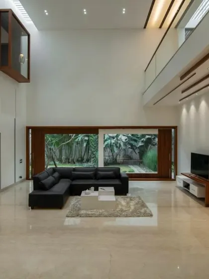 A double-height living room that emphasizes volume and light. A large window connects the space to an outdoor garden, while the minimalist furniture keeps the focus on the grand architectural scale.