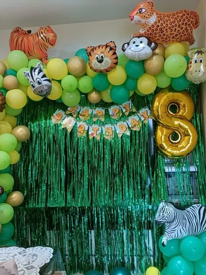 A jungle-themed 8th birthday party setup for a home. It features a green fringe backdrop and a balloon arch decorated with animal-shaped foil balloons.
