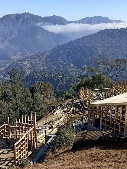 An overview of the Vasudev site, showing the timber skeletons of the guesthouses taking shape against the vast mountain landscape. The project is a collection of small structures designed to feel like a natural extension of the village.