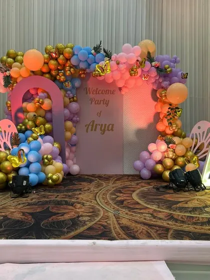 Another angle of Arya's butterfly-themed party stage. The lighting highlights the beautiful mix of orange, blue, purple, and gold balloons, creating a warm and festive atmosphere.
