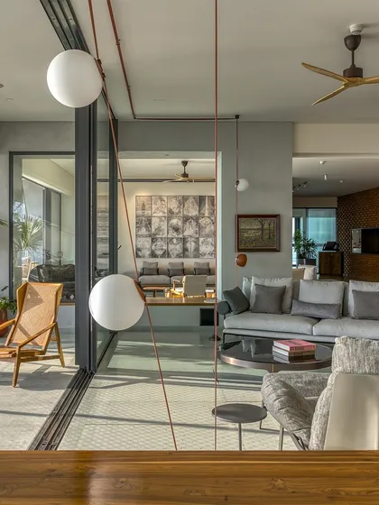 The living room of Sampurna Residence features custom lighting and a mix of modern furniture, creating a relaxed atmosphere with a connection to the sunlit verandah.