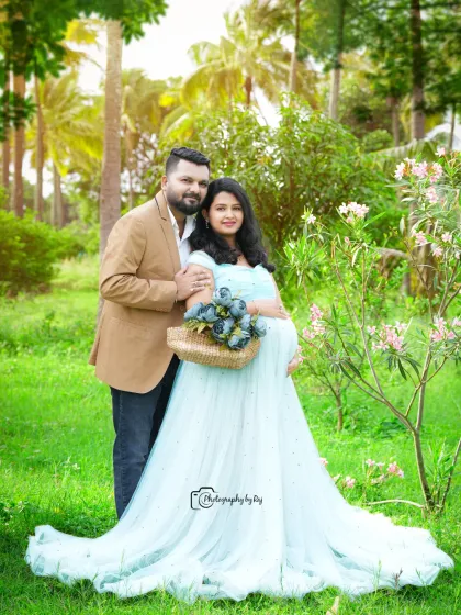 A lovely couple's portrait in a garden, with the mother-to-be in a light blue gown holding a basket of flowers.