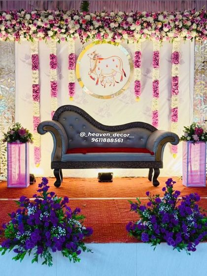 A beautiful stage for a Seemantha or baby shower ceremony. The decor features a custom backdrop with a traditional cow motif, symbolizing motherhood, framed by elegant floral arrangements in purple and white.
