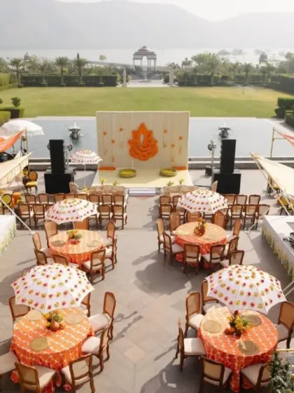 An aerial view of a traditional Haldi setup, featuring tables shaded by custom-printed umbrellas. The layout is designed for both aesthetic appeal and guest comfort, with a floral Ganesha as the centerpiece.