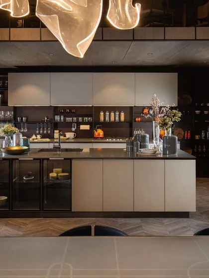 Our kitchen designs are engineered for high utility without compromising on aesthetics. This open-plan kitchen features an expansive island with an integrated glass crockery unit, ample backsplash storage, and a seamless blend of neutral tones and dark accents.