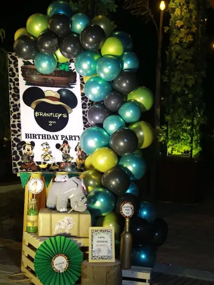 A welcome setup for the birthday party, featuring a personalized sign, a balloon garland, and themed props like a small elephant figure, all arranged on rustic wooden crates.