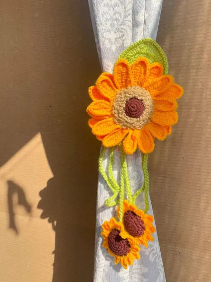A close-up of the sunflower curtain tie in action. The bright yellow flower and dangling smaller sunflowers create a lovely, cascading effect.