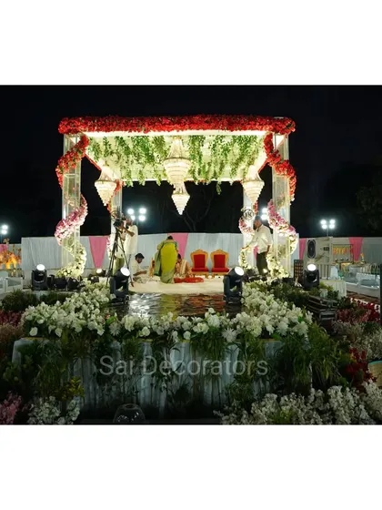 A classic engagement mandap setup for an outdoor venue. The structure is adorned with red and white flowers and features a beautiful chandelier, creating a traditional and sacred space for the ceremony.