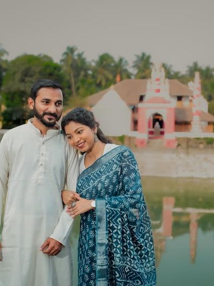 A happy portrait of the couple in front of a traditional temple. The bride leans on her partner's arm, both smiling, capturing a moment of shared faith and love.