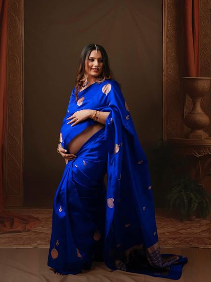 Draped in elegance and stories. This mom-to-be looks absolutely regal in her royal blue saree, set against a classic, fine art backdrop.