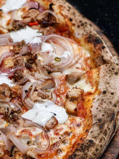A close-up view of the Bird in Hand pizza, focusing on the texture of the toppings and the perfectly charred sourdough crust.