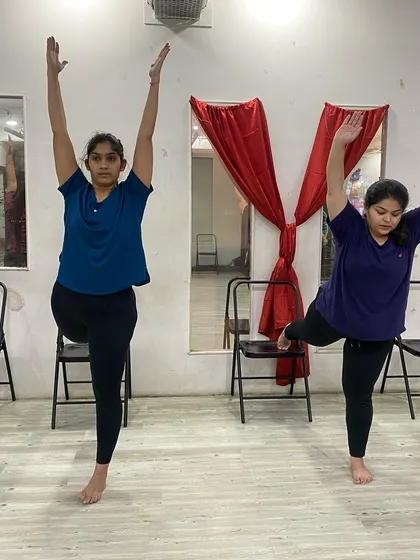 Practicing a standing balance pose with the support of a chair, making it accessible for all fitness levels.