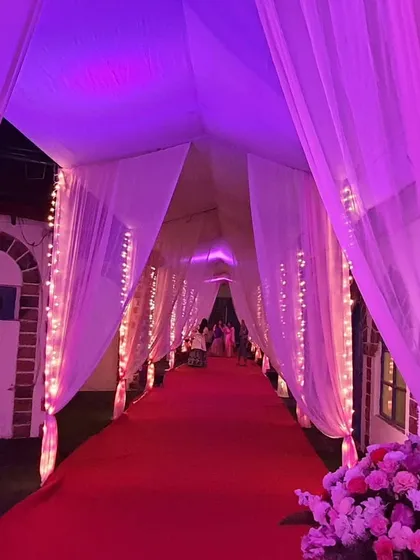 A dramatic entrance created with a red carpet and a tunnel of white drapes. The entire passage is bathed in purple and pink uplighting, setting a glamorous and high-energy mood for the celebration.