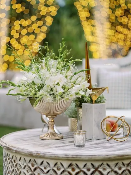 A centerpiece with white florals and gold accents against a backdrop of twinkling lights. The warm glow creates a cozy and inviting atmosphere for guests.