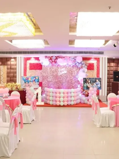 A wide view of a first birthday party setup in a hall, featuring a sequin wall backdrop and pink-themed table settings.