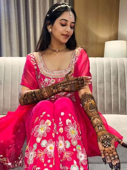 A beautiful bride in a bright pink outfit, showing her intricate bridal mehandi.
