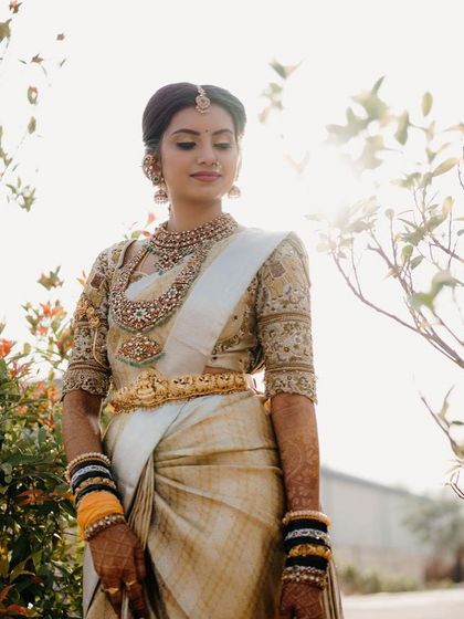 A bride in a white and gold Kanchipuram saree, paired with a blouse featuring intricate elephant and floral embroidery.