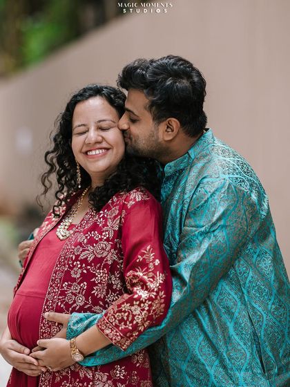 A sweet kiss and a happy smile. This candid shot captures the genuine affection between the couple during their maternity session, dressed in beautiful traditional Indian attire.