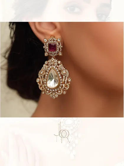 A pair of magnificent statement earrings, with a large uncut diamond drop set in an ornate, diamond-studded frame with a ruby accent.